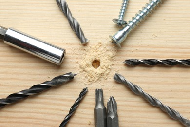 Different drill bits on holed wooden surface, flat lay