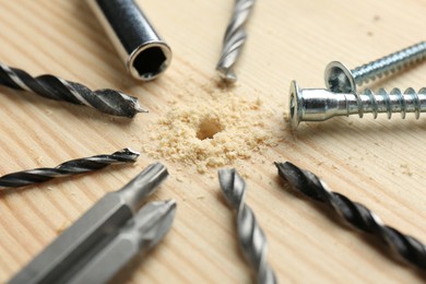 Photo of Different drill bits on holed wooden surface, closeup