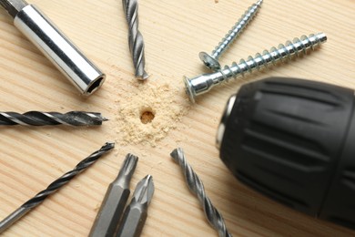 Different bits and cordless electric drill on holed wooden surface, closeup