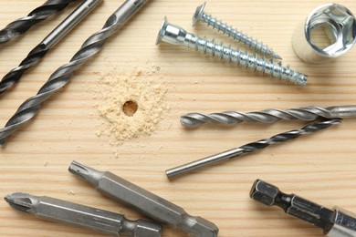 Photo of Different drill bits on holed wooden surface, flat lay