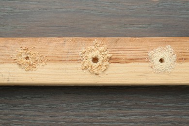 Photo of Plank with holes and sawdust on wooden table, top view