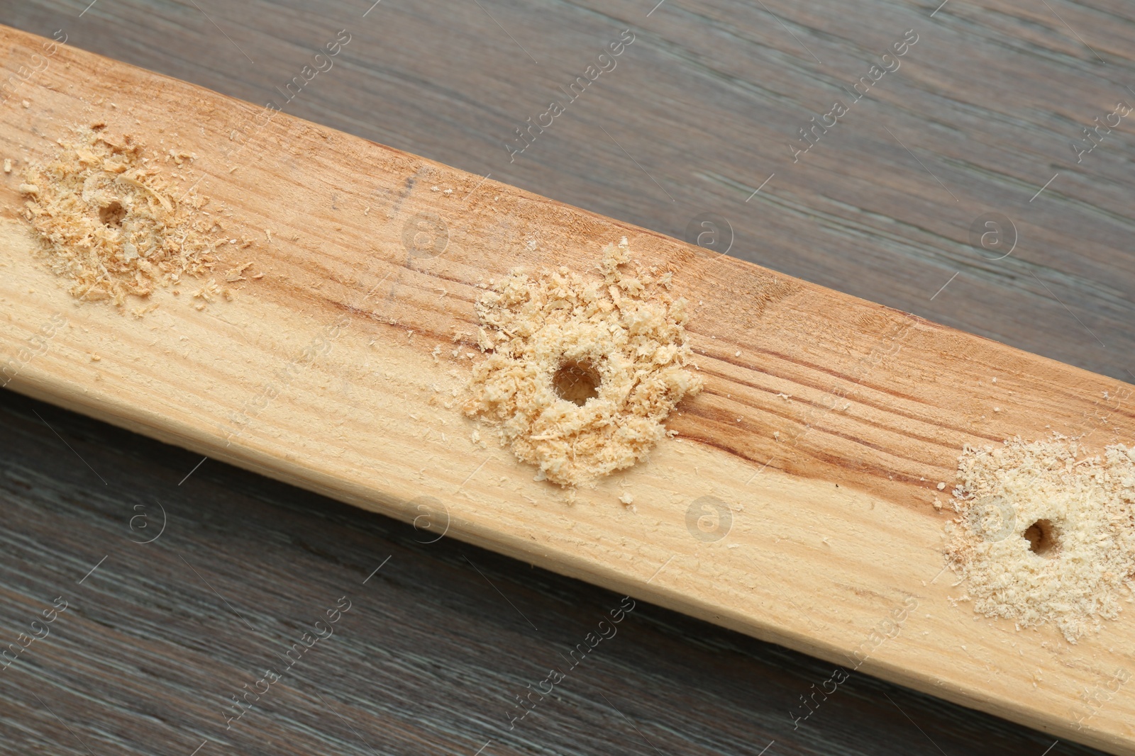 Photo of Plank with holes and sawdust on wooden table, top view