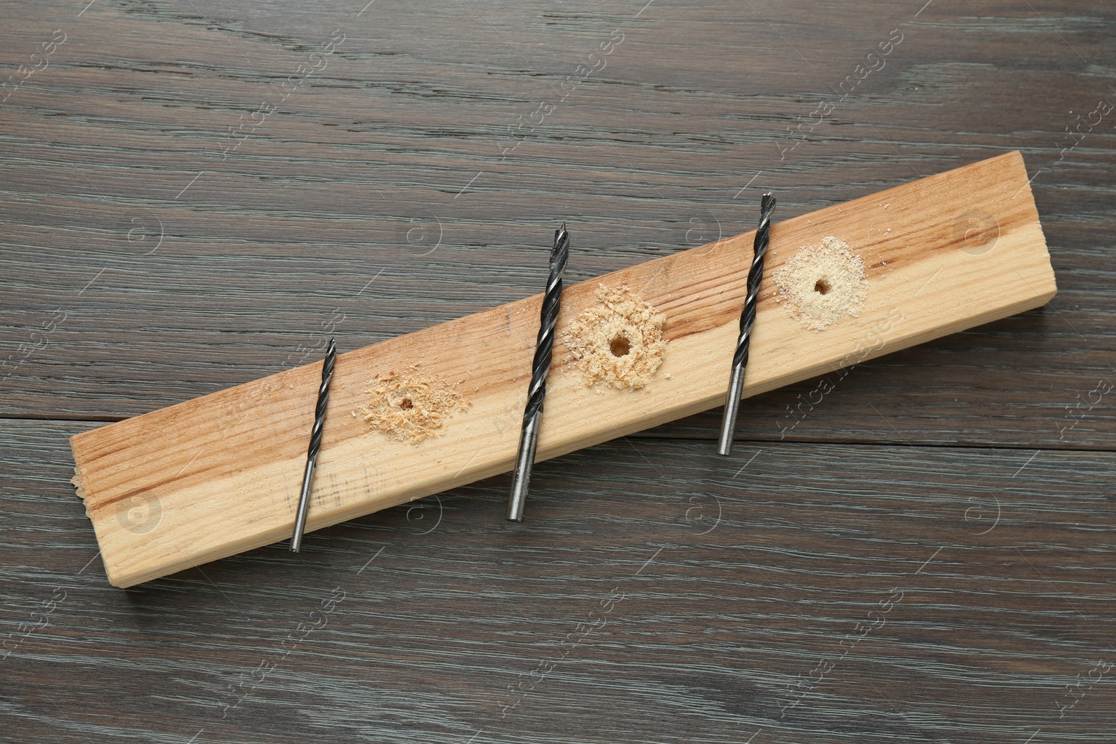 Photo of Plank with holes, drill bits and sawdust on wooden table, flat lay