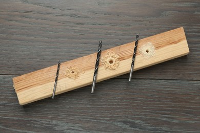 Plank with holes, drill bits and sawdust on wooden table, flat lay