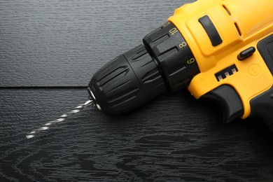 Photo of Cordless electric drill on black wooden table, top view