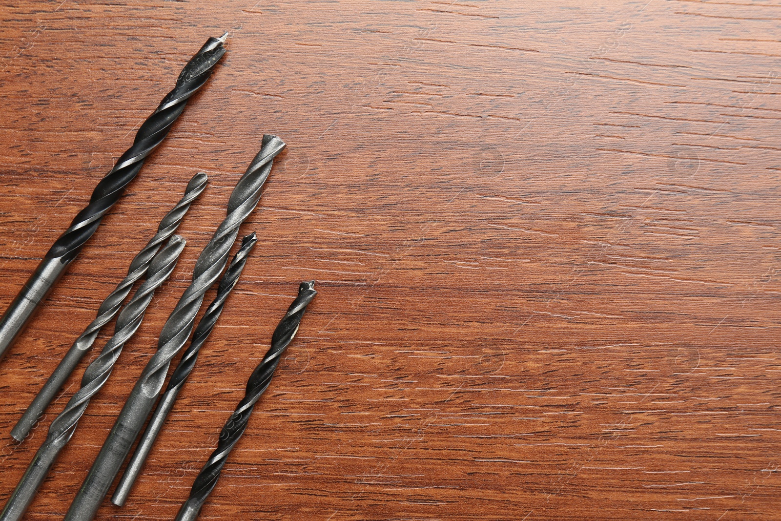 Photo of Many drill bits on wooden table, flat lay. Space for text