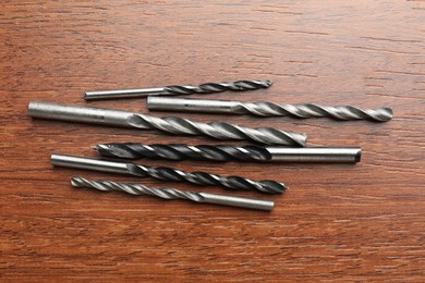 Many drill bits on wooden table, flat lay