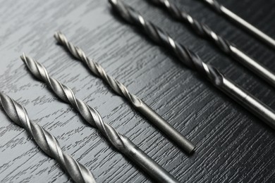 Many drill bits on black wooden table, closeup