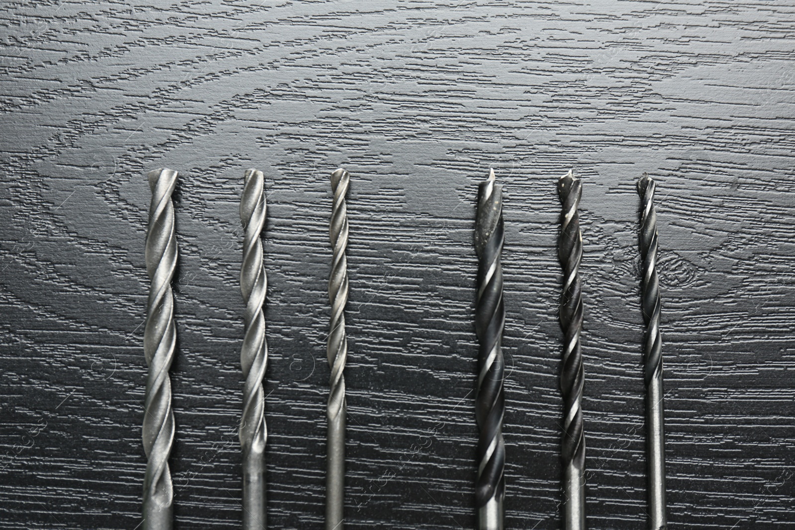 Photo of Many drill bits on black wooden table, flat lay