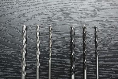 Photo of Many drill bits on black wooden table, flat lay