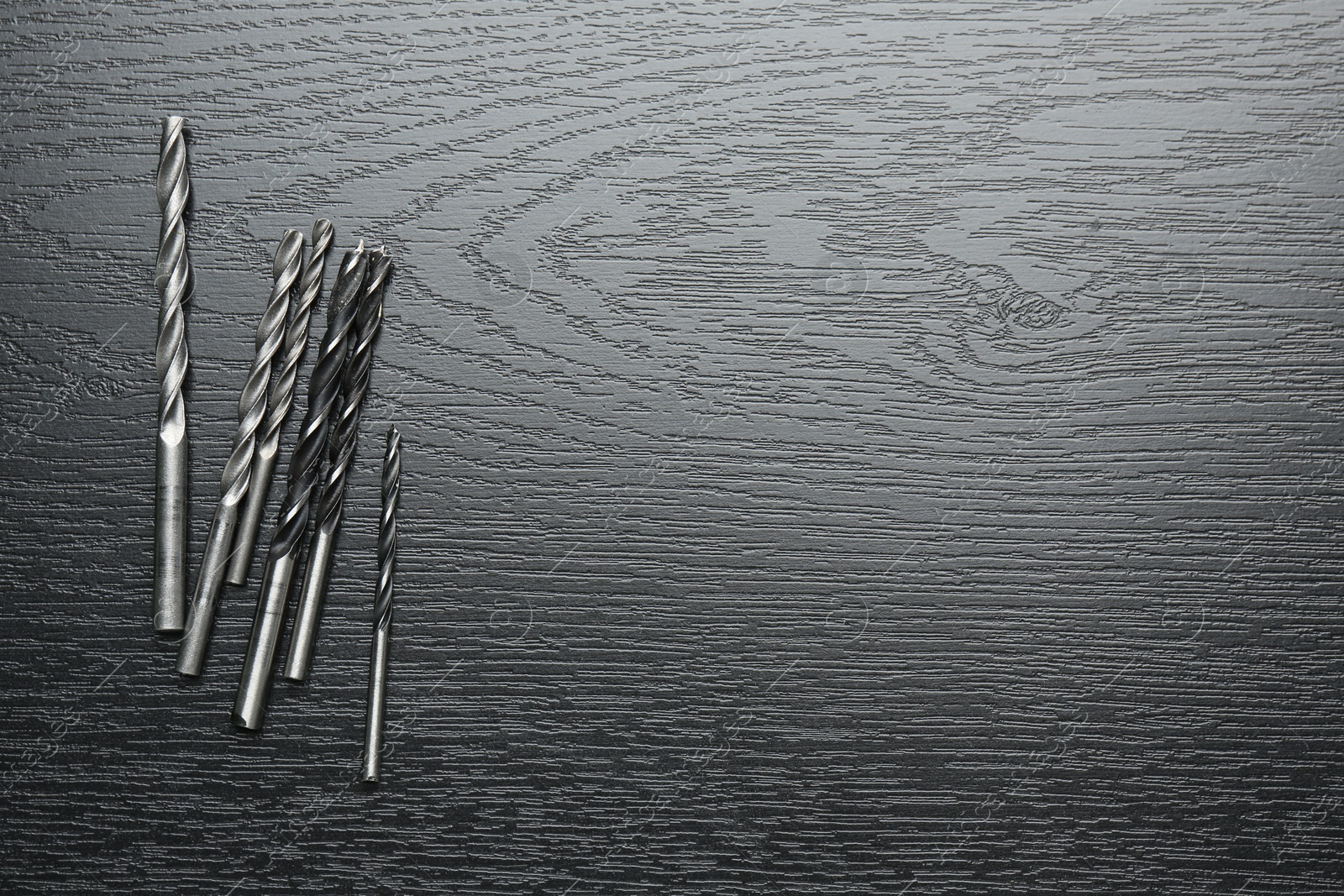 Photo of Many drill bits on black wooden table, flat lay. Space for text