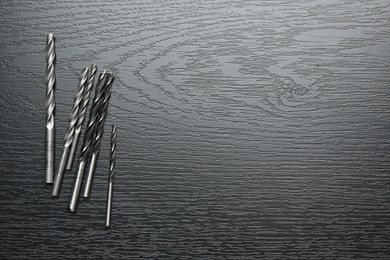 Photo of Many drill bits on black wooden table, flat lay. Space for text