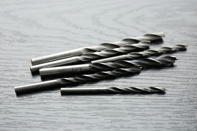 Many drill bits on black wooden table, closeup