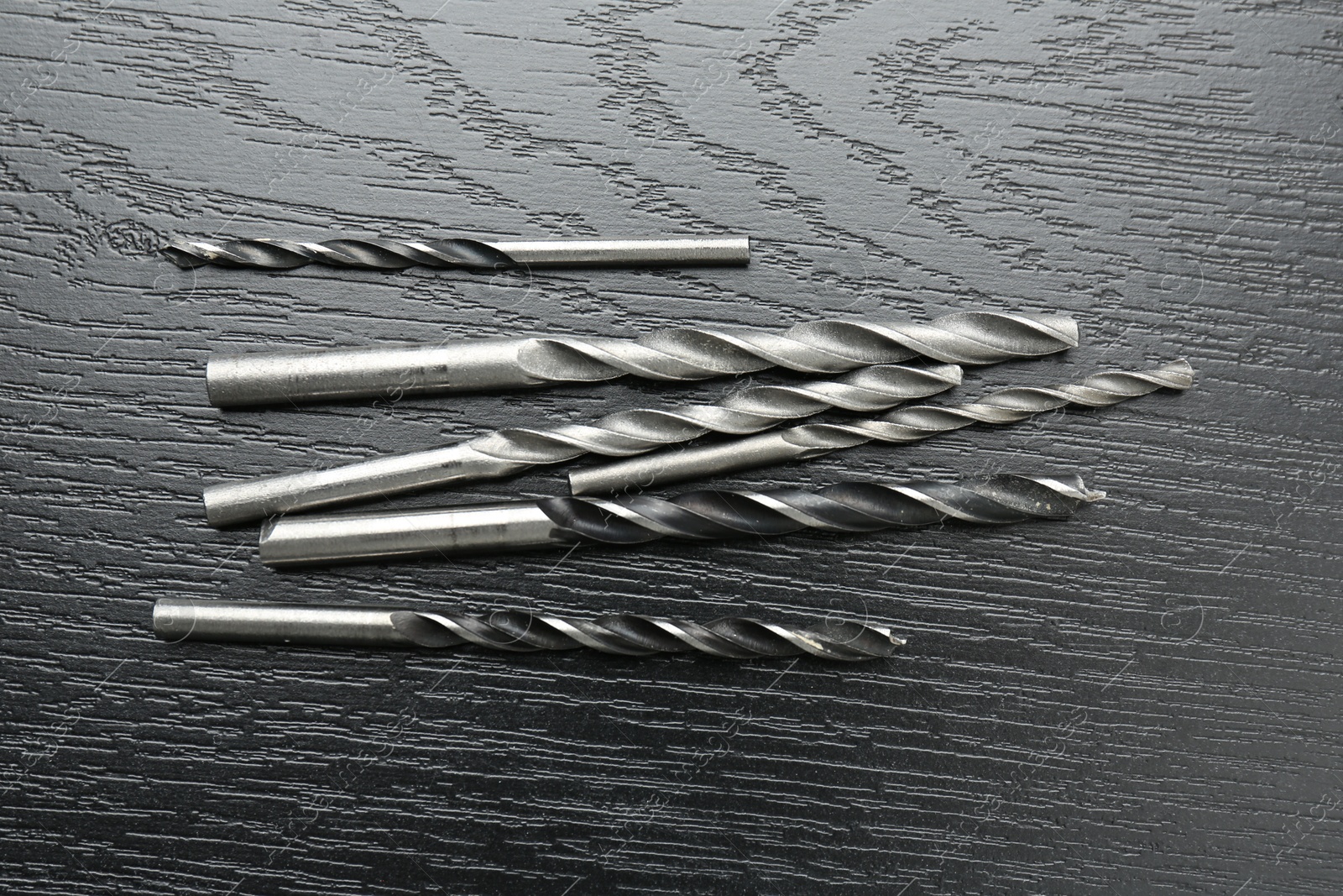 Photo of Many drill bits on black wooden table, flat lay