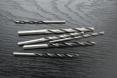 Photo of Many drill bits on black wooden table, flat lay