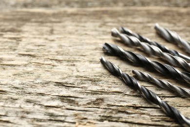 Many drill bits on wooden table, closeup. Space for text