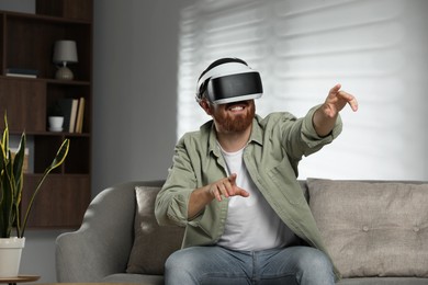 Photo of Smiling man using virtual reality headset on sofa at home