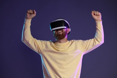 Photo of Smiling man using virtual reality headset on dark purple background