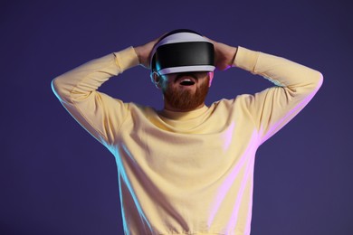 Photo of Surprised man using virtual reality headset on dark purple background