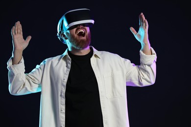 Photo of Emotional man using virtual reality headset on dark background in neon lights