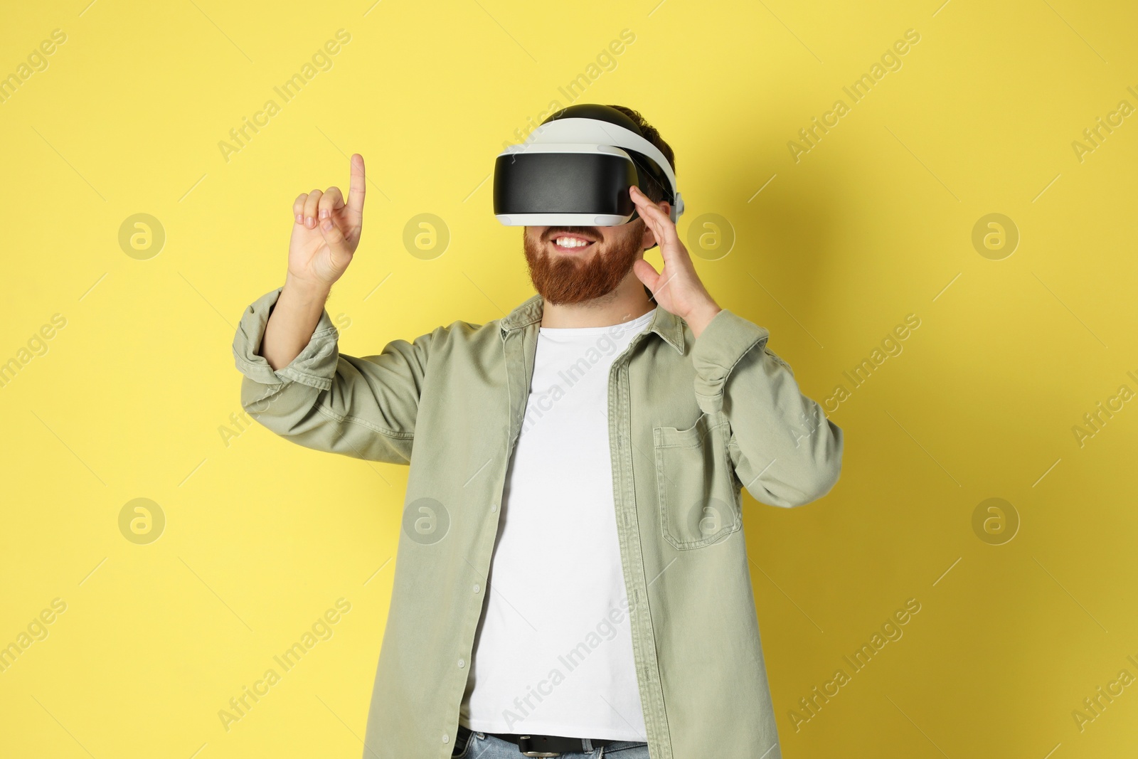 Photo of Happy man using virtual reality headset on pale yellow background