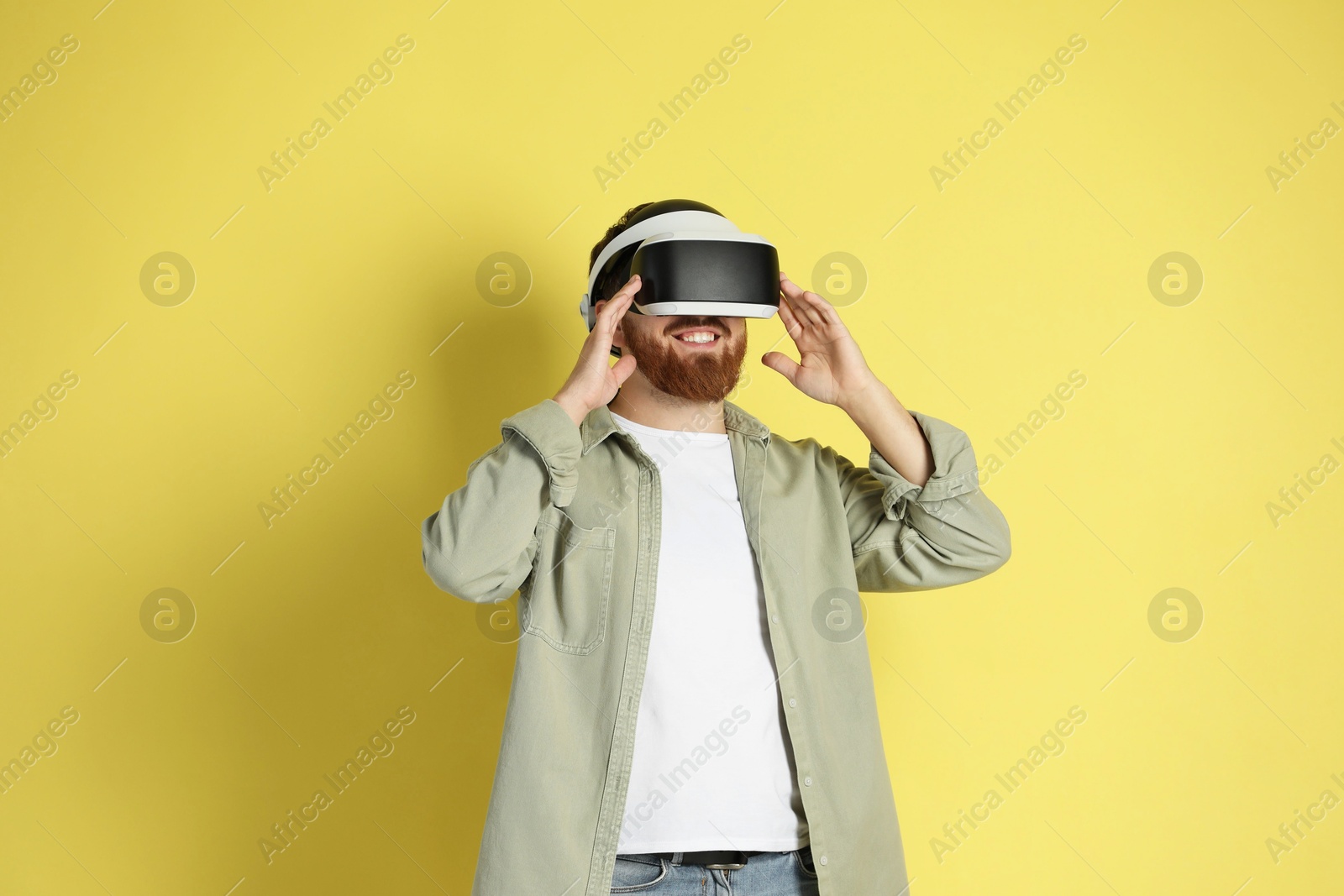 Photo of Happy man using virtual reality headset on pale yellow background