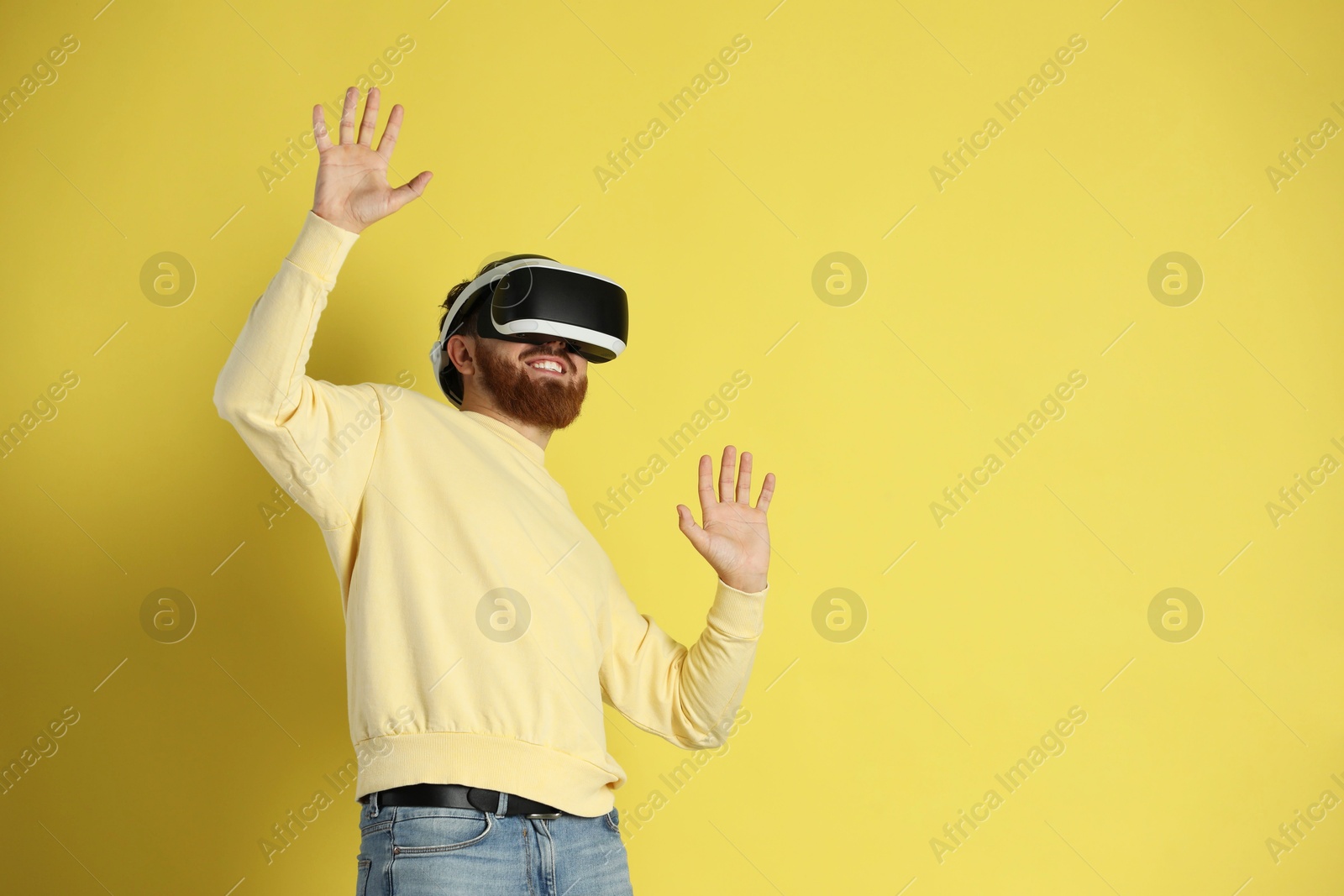 Photo of Happy man using virtual reality headset on pale yellow background. Space for text