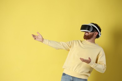 Photo of Happy man using virtual reality headset on pale yellow background. Space for text