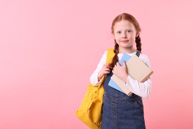 Photo of Cute little girl with books and backpack on pink background. Space for text