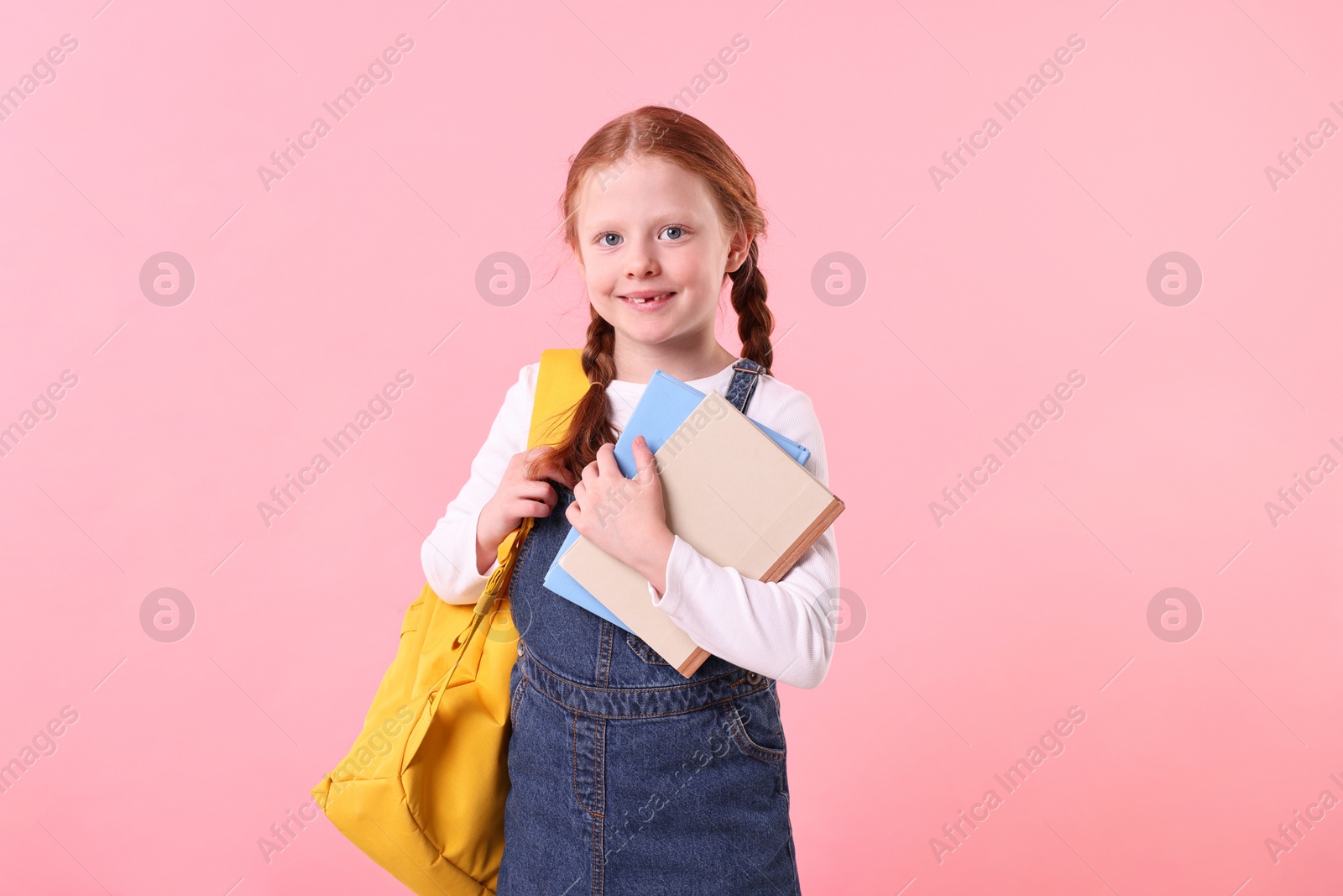 Photo of Smiling little girl with books and backpack on pink background