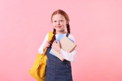 Photo of Smiling little girl with books and backpack on pink background