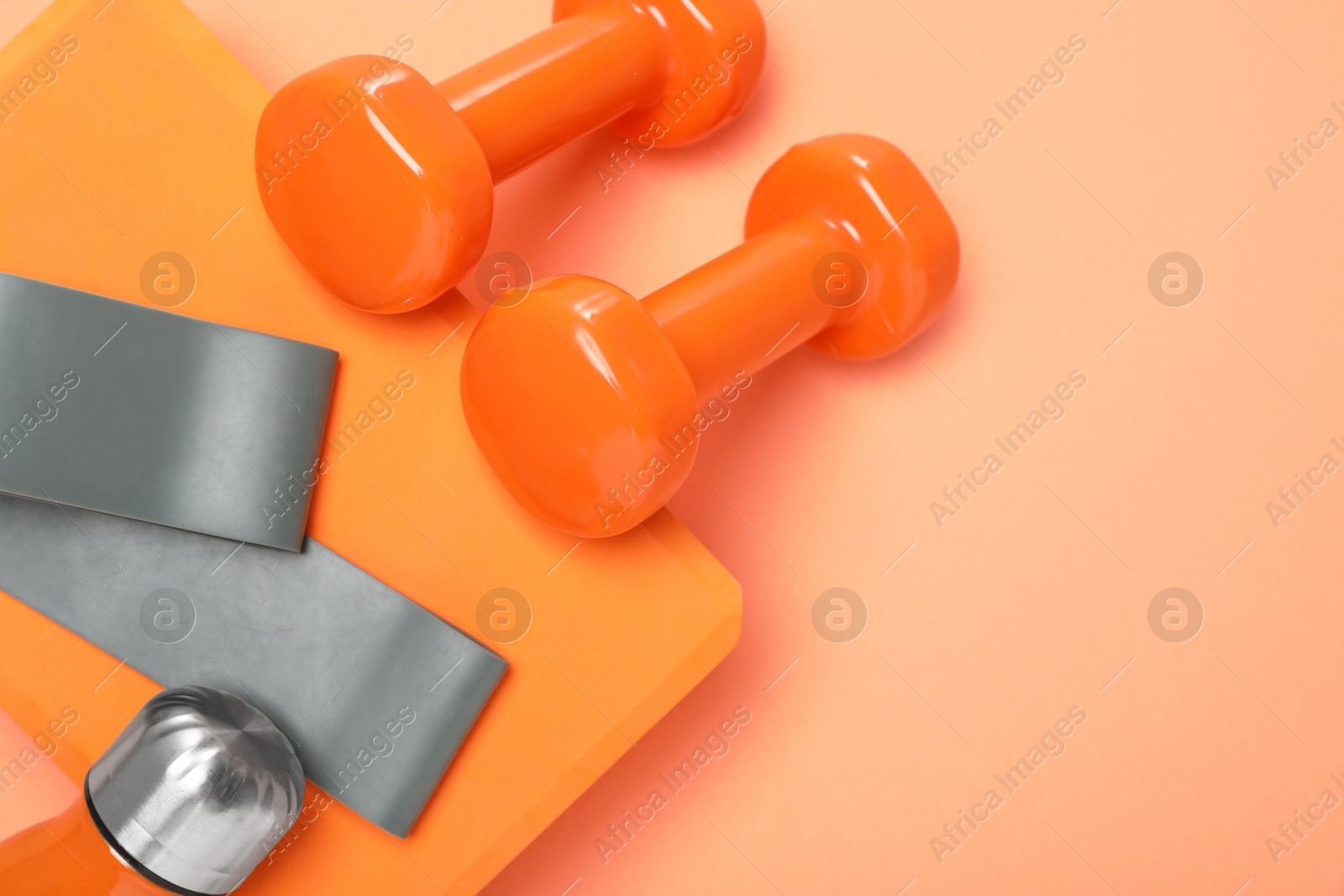 Photo of Dumbbells, thermo bottle, fitness elastic band and yoga block on coral background, flat lay. Space for text