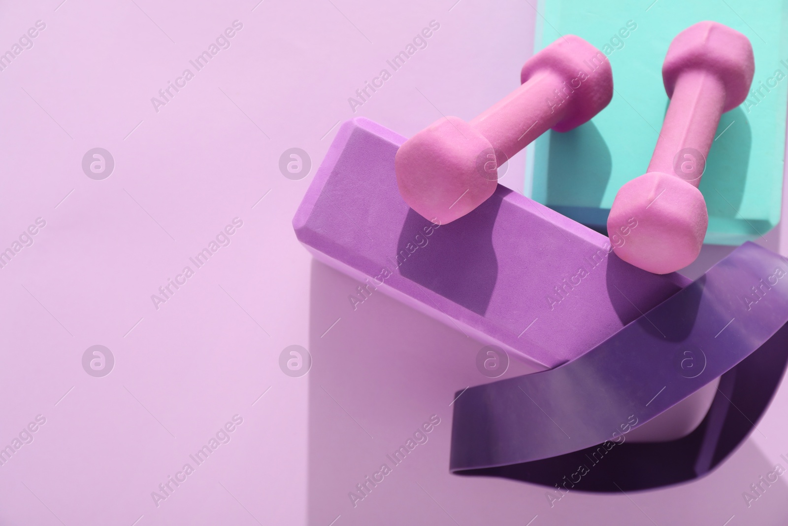 Photo of Two dumbbells, yoga blocks and fitness elastic band on violet background, flat lay. Space for text