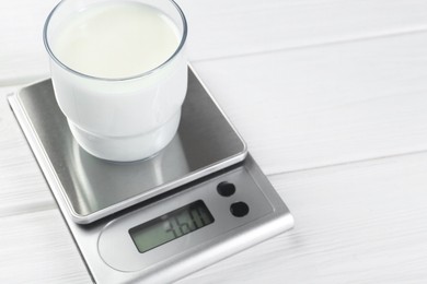 Photo of Kitchen scale with glass of milk on white wooden table, closeup. Space for text