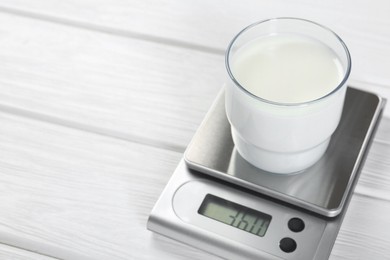 Photo of Kitchen scale with glass of milk on white wooden table, closeup. Space for text