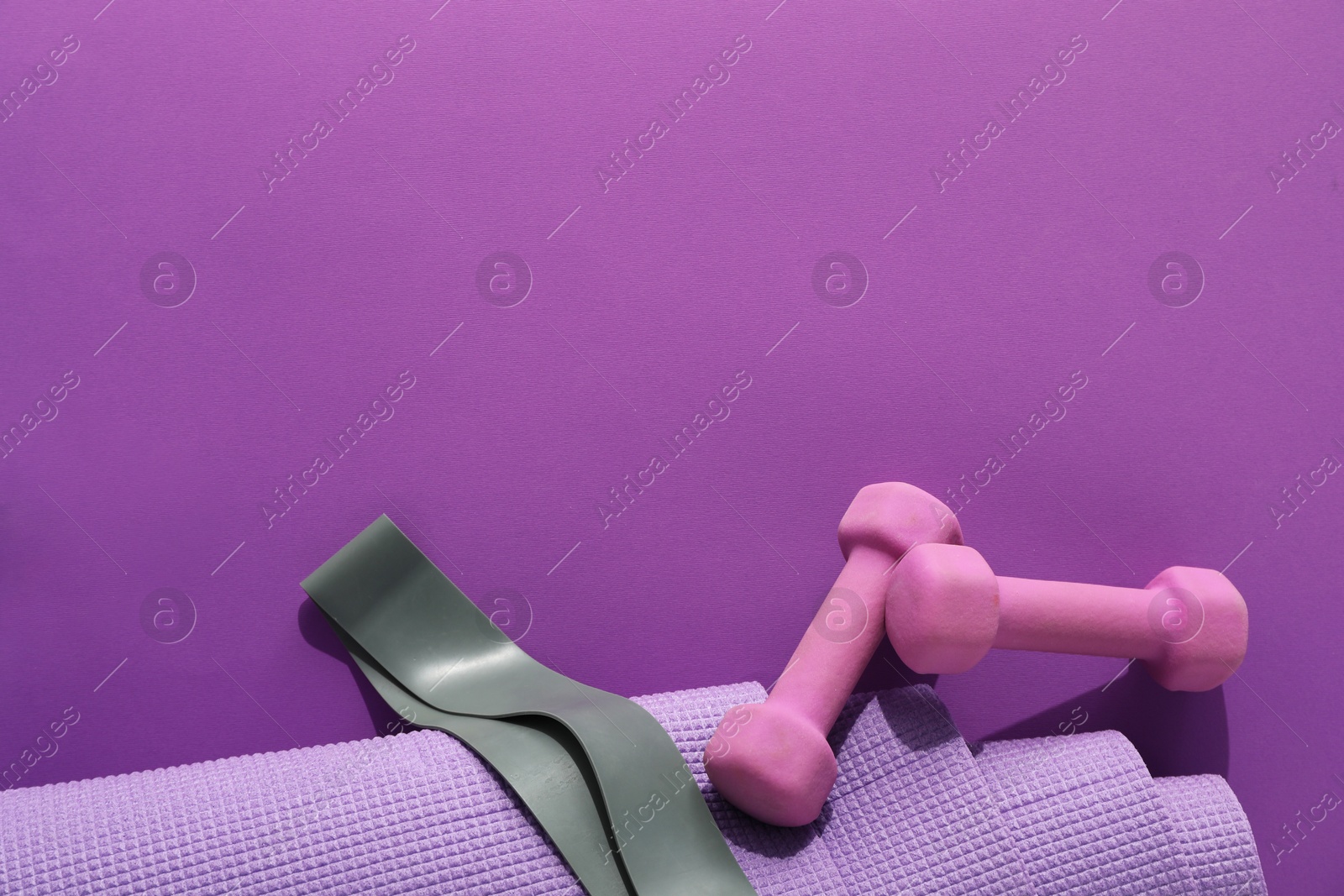 Photo of Dumbbells, yoga mat and fitness elastic band on purple background, flat lay. Space for text