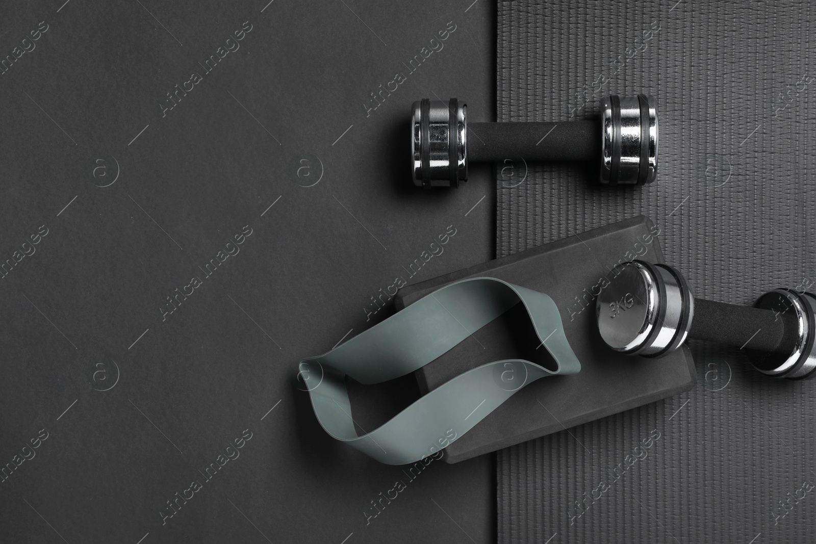 Photo of Dumbbells, yoga block, mat and fitness elastic band on black background, flat lay. Space for text