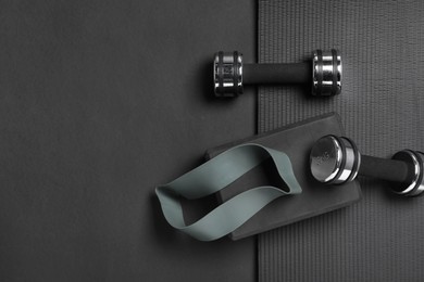Photo of Dumbbells, yoga block, mat and fitness elastic band on black background, flat lay. Space for text