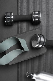 Photo of Dumbbells, yoga block, mat, thermo bottle and fitness elastic band on black background, flat lay