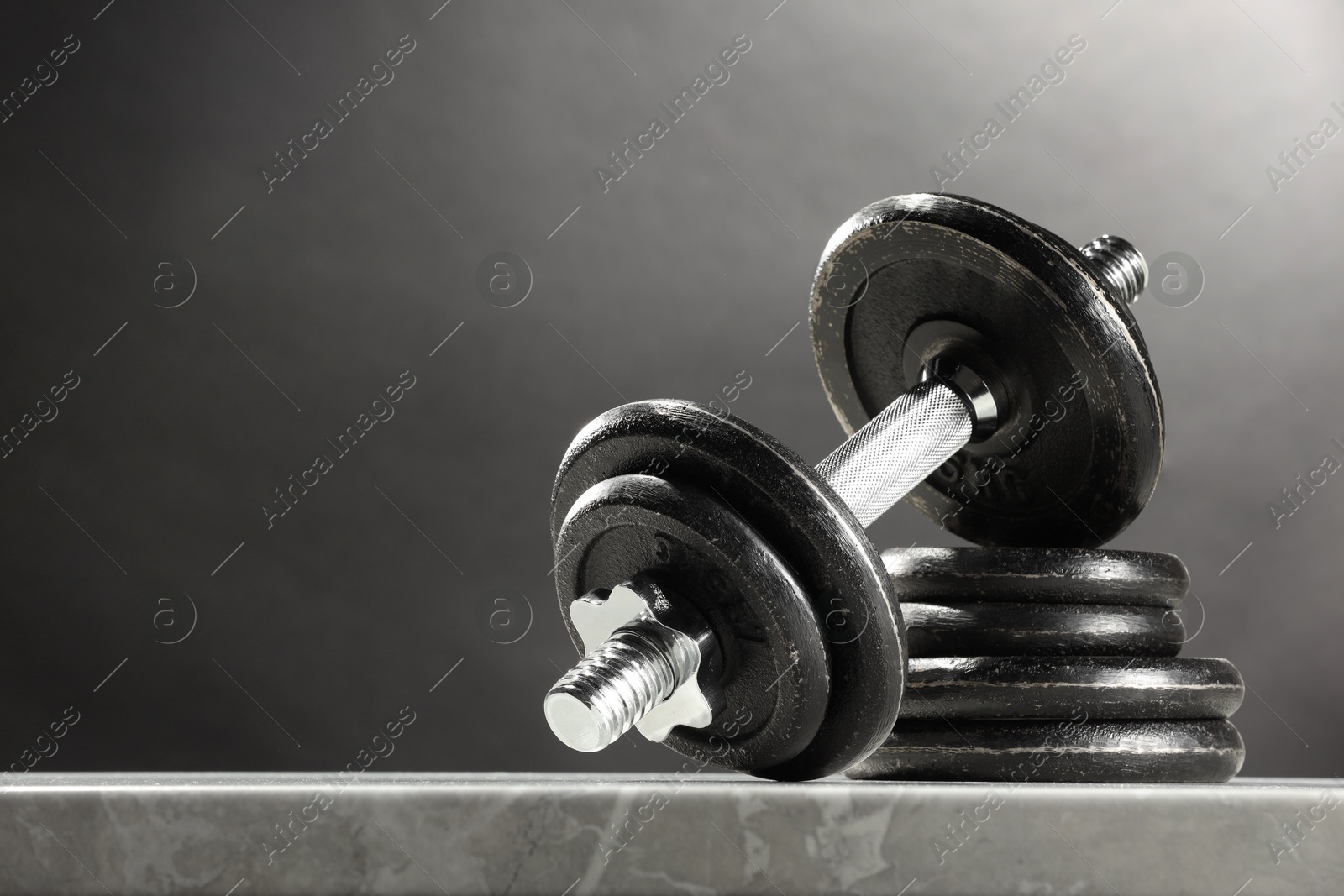 Photo of Barbell and stack of plates on marble table against dark background. Space for text