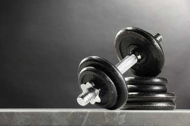 Photo of Barbell and stack of plates on marble table against dark background. Space for text