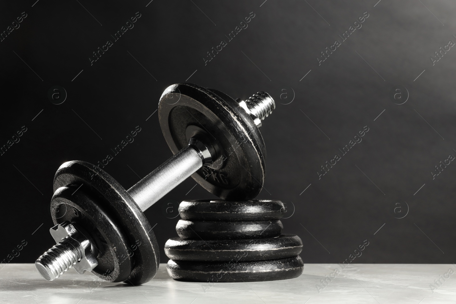 Photo of Barbell and stack of plates on light table against dark background. Space for text