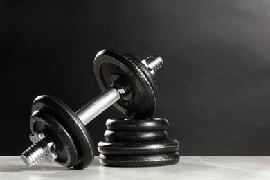 Photo of Barbell and stack of plates on light table against dark background. Space for text