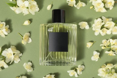 Photo of Aromatic perfume in bottle among beautiful jasmine flowers on pale green background, flat lay