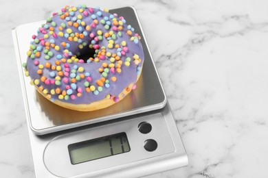 Photo of Kitchen scale with donut on white marble table, closeup