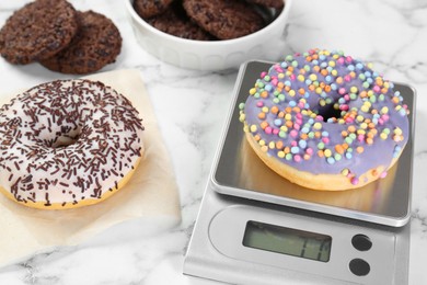 Photo of Kitchen scale with donut on white marble table, closeup