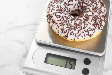 Photo of Kitchen scale with donut on white marble table, closeup