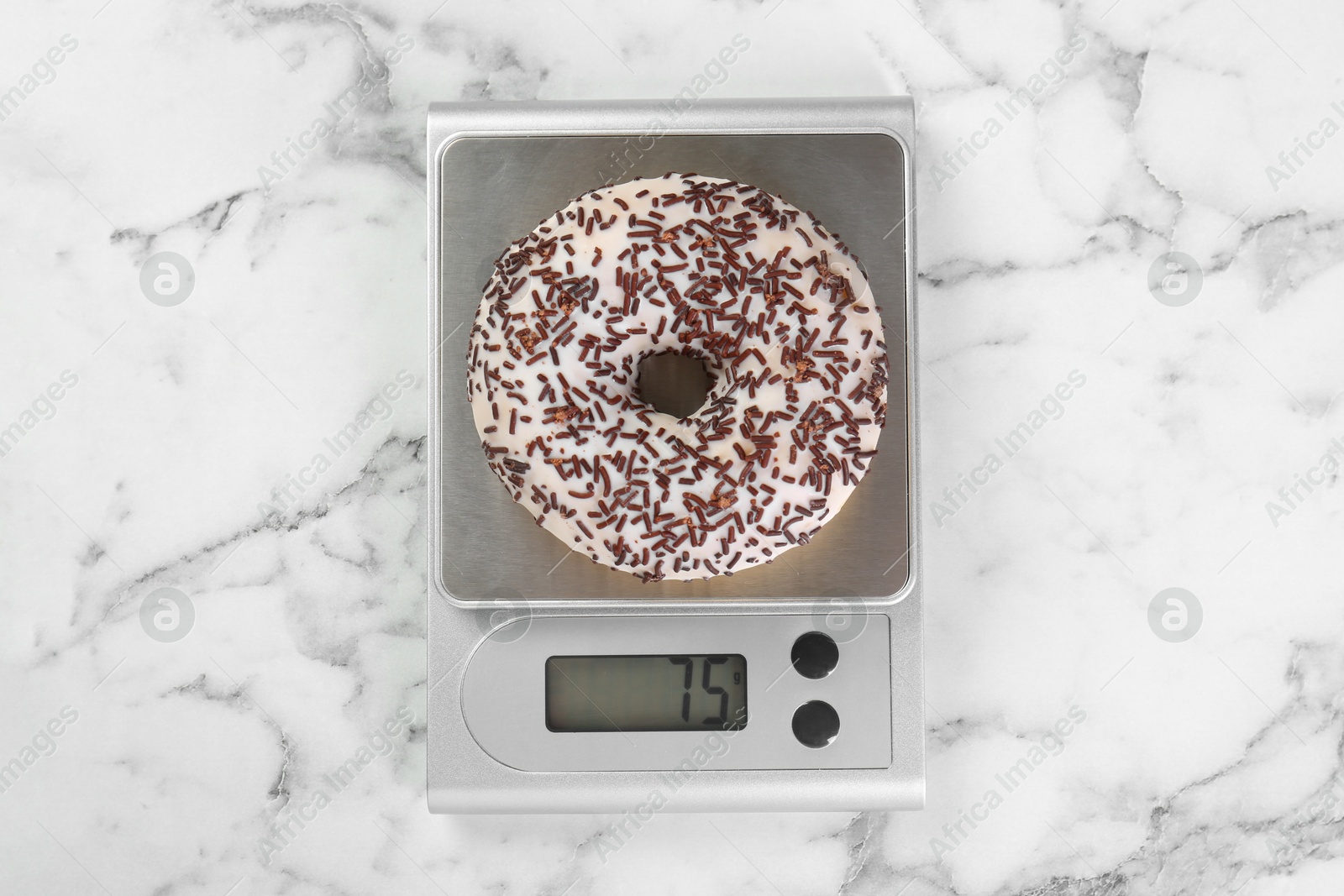 Photo of Kitchen scale with donut on white marble table, top view