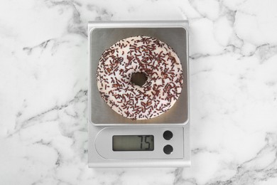 Photo of Kitchen scale with donut on white marble table, top view