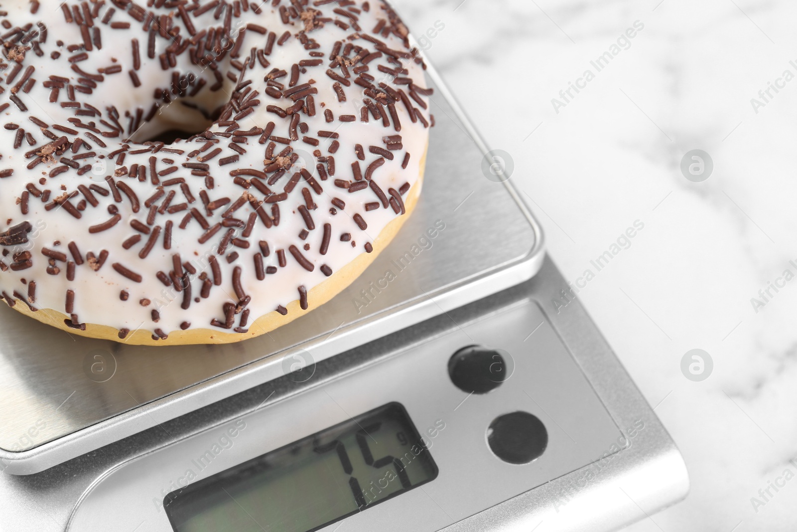 Photo of Kitchen scale with donut on white marble table, closeup